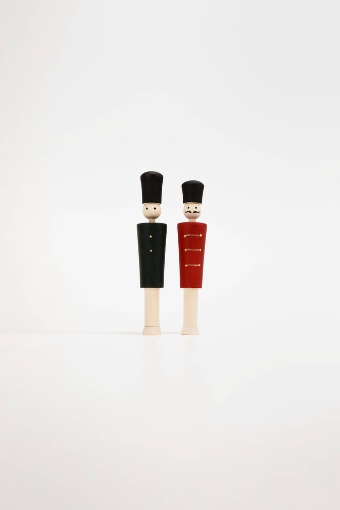 The pair of "Wooden Soldiers," clad in tall hats, stand side by side against a light background as if guarding a hidden advent calendar. One wears a green uniform and the other a red one, both adorned with simply painted features.