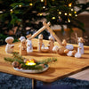The Wooden Nativity Scene, crafted in Germany, is displayed on a table with Mary, Joseph, baby Jesus, animals, and more. A glowing Christmas tree stands behind it while a tray with candles and greenery adorns the foreground.