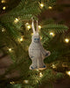 The Coral & Tusk Yeti with Candy Cane Ornament, featuring embroidered details, hangs on a green Christmas tree branch with glowing white lights—a charming holiday decoration and perfect Christmas gift.