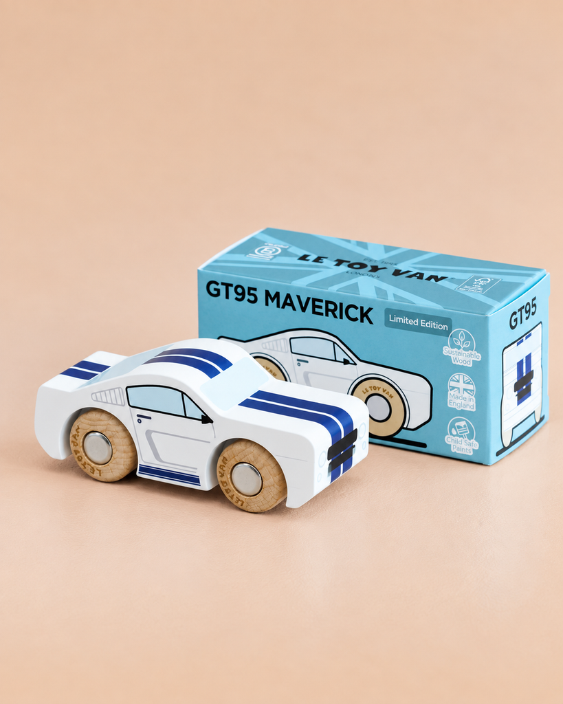 A white wooden toy car with blue stripes, inspired by iconic muscle car designs, is displayed next to its blue packaging box labeled “No. 17 GT95 Maverick | Made in England” on a beige surface.