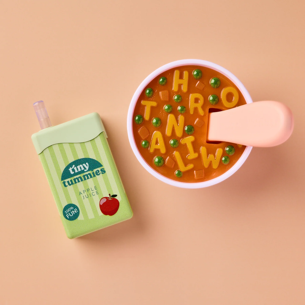 The Tiny Tummies Set - Alphabet Soup Bowl and Juice Box For Dolls features a bowl of alphabet soup with peas and a pink spoon, alongside a green juice box labeled “tiny tummies apple juice,” all set against a peach background. Perfect for play sets or as doll accessories, the soup contains letter shapes including H, R, O, T, A, N, I, and W.