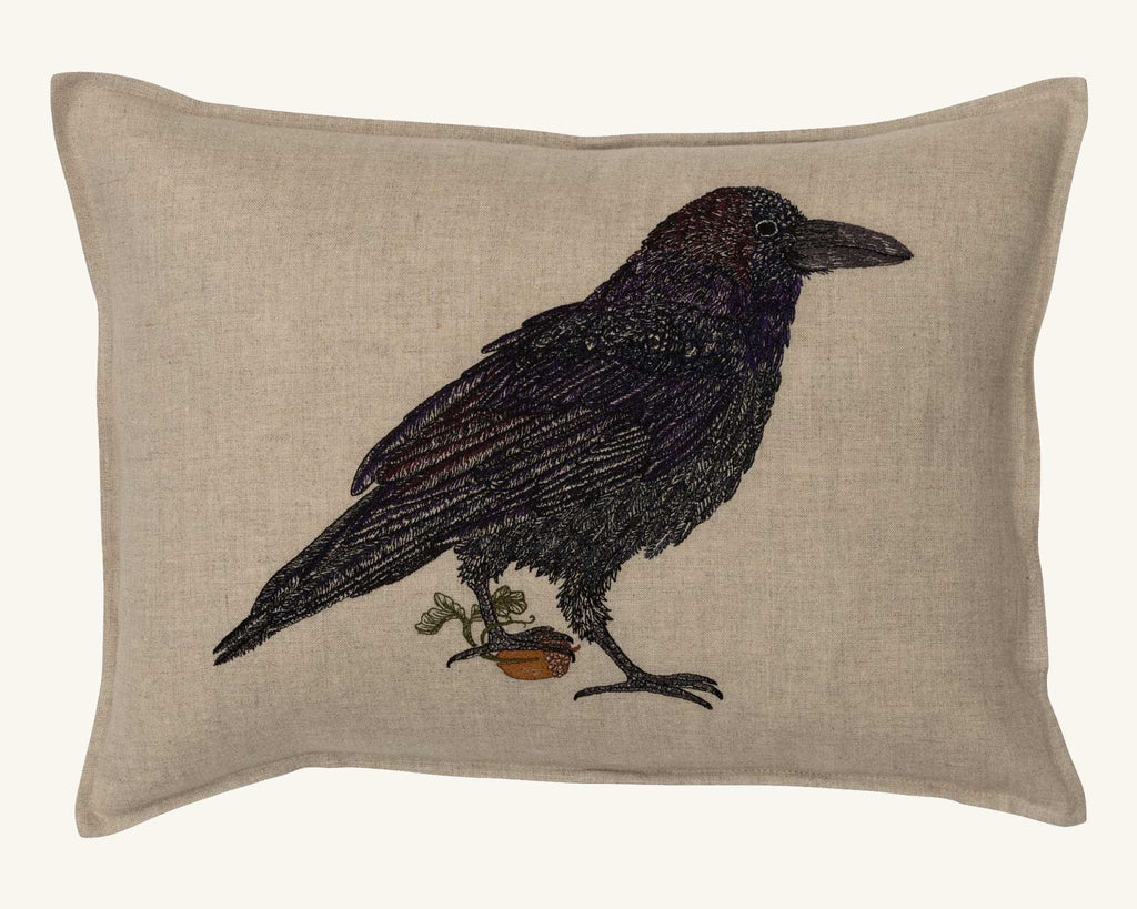 The Coral & Tusk Blackbird with Acorn Pillow showcases an embroidered blackbird next to a potted plant on beige Oeko-Tex certified linen.