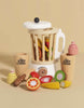 The Fruit & Smoothie Blender Set includes a wooden toy blender, sliceable apple, kiwi, banana, and orange pieces, two cups, a knife, and bottles—ideal for any toy kitchen. Displayed on a beige surface with a beige background.