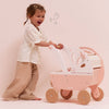 A young girl laughs as she pushes a pink wooden Retro Wooden Doll Stroller decorated with a butterfly motif.