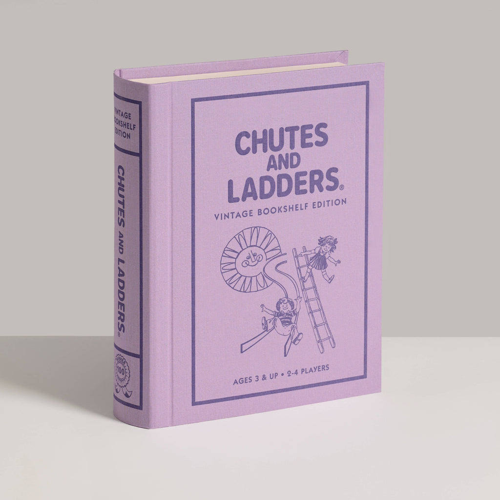 A lavender "Chutes and Ladders Vintage Bookshelf Edition" book stands upright, its cover featuring line drawings of children playing—reflecting the charm of this classic board game for ages 3 and up.
