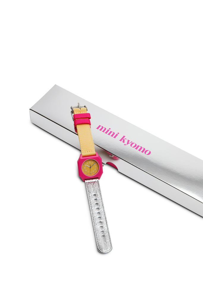 The Mini Kyomo Watch - Disco, featuring a pink face and yellow strap, is shown next to a silver box labeled “mini kyomo” in pink text.
