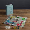 The Sorry! Vintage Bookshelf Edition is displayed on a wooden table with colorful pieces, cards, and its book-shaped collectible box standing upright in the background.