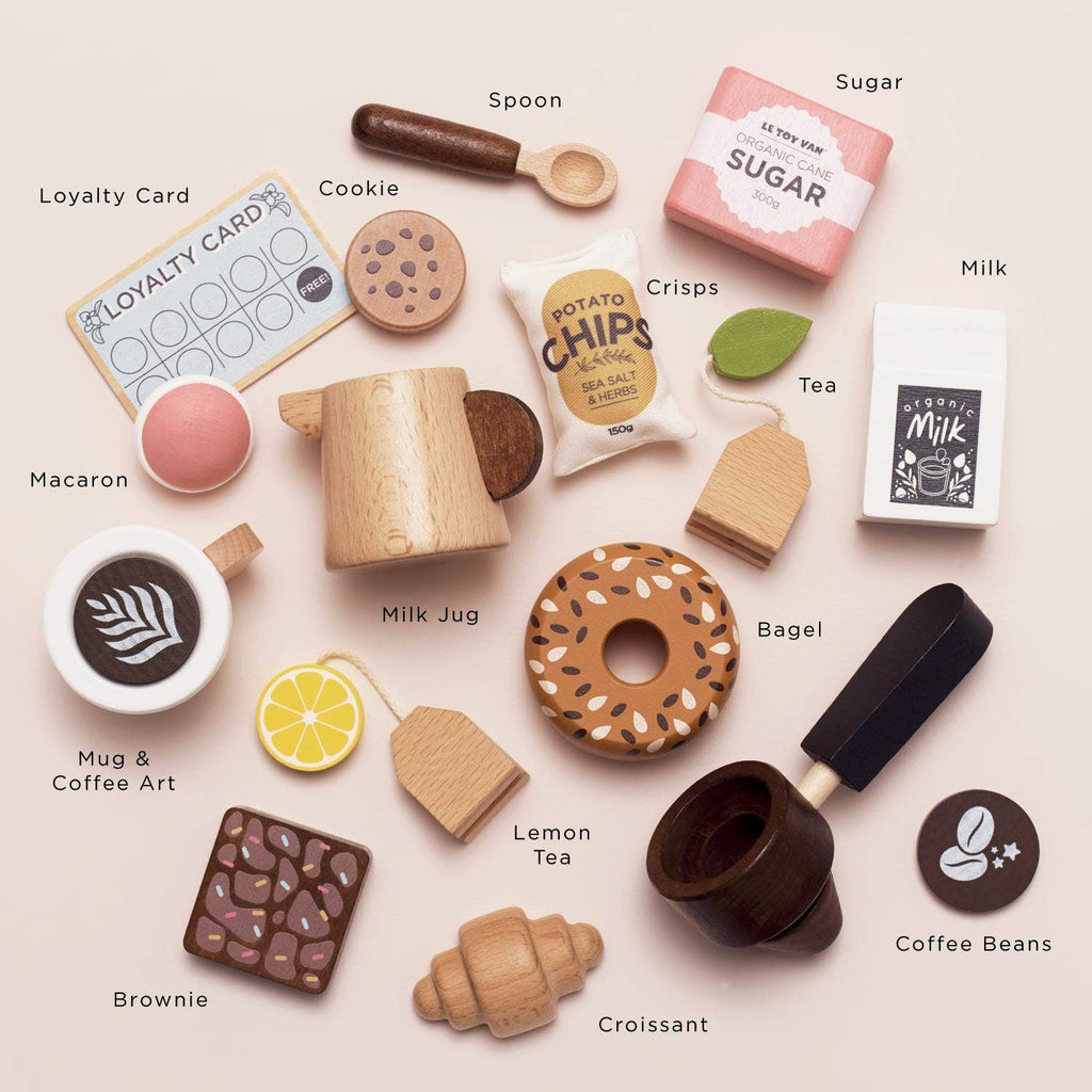 A flat lay of wooden toy food and drinks labeled with names from the Barista Café Shop set (ships in one week), including a loyalty card, cookie, spoon, sugar, crisps, milk jug, bagel, lemon tea, coffee mug with art, croissant, and brownie.