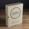 A beige Scrabble Vintage Bookshelf Edition box, styled like a book for ages 8+, suited for 2-4 players, stands upright on a wooden surface and features premium game components.