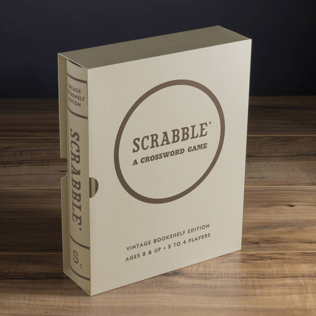 A beige Scrabble Vintage Bookshelf Edition box, styled like a book for ages 8+, suited for 2-4 players, stands upright on a wooden surface and features premium game components.