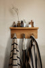 The Ferm Living Place Rack - Small, styled with bottles, jars, and vases on top and three striped towels plus a mesh bag hanging below, is perfect for chic home organization against a beige wall.