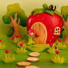 A whimsical scene with a strawberry house, tulips, trees, and stepping stones features the Bumbu Handmade Wooden Flower Child Tulip (ships in one week), perfect for open-ended play as a bee hovers above.