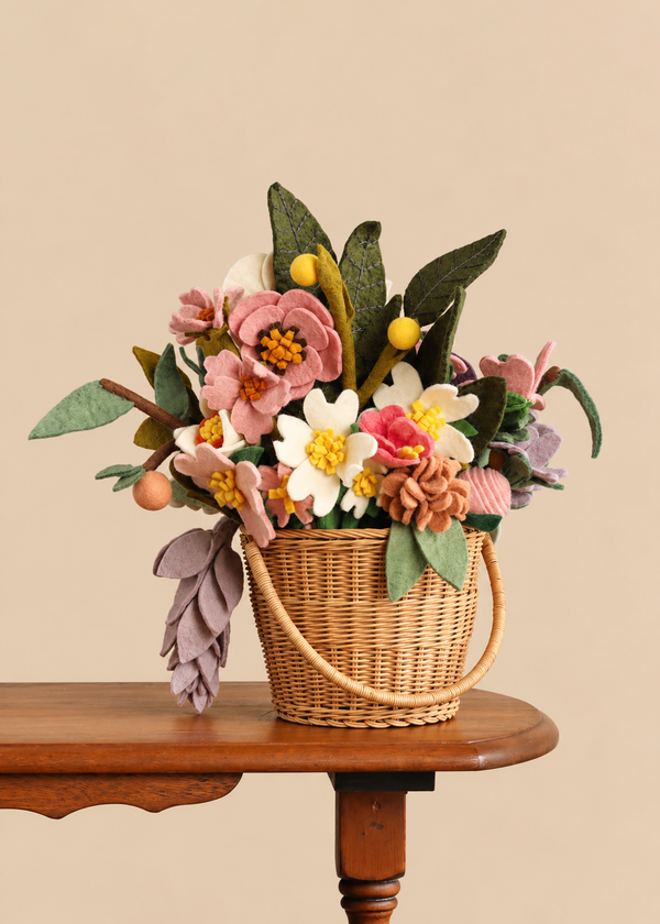 Basket of Handmade Felt Flowers - Final Sale featuring a colorful felt flower arrangement and green leaves in a woven basket on a wooden table.