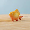 The Bumbu Handmade Wooden Golden Fish, a small orange and yellow Montessori Waldorf toy with painted scales and fins, rests on a light wooden surface against a soft blue background.