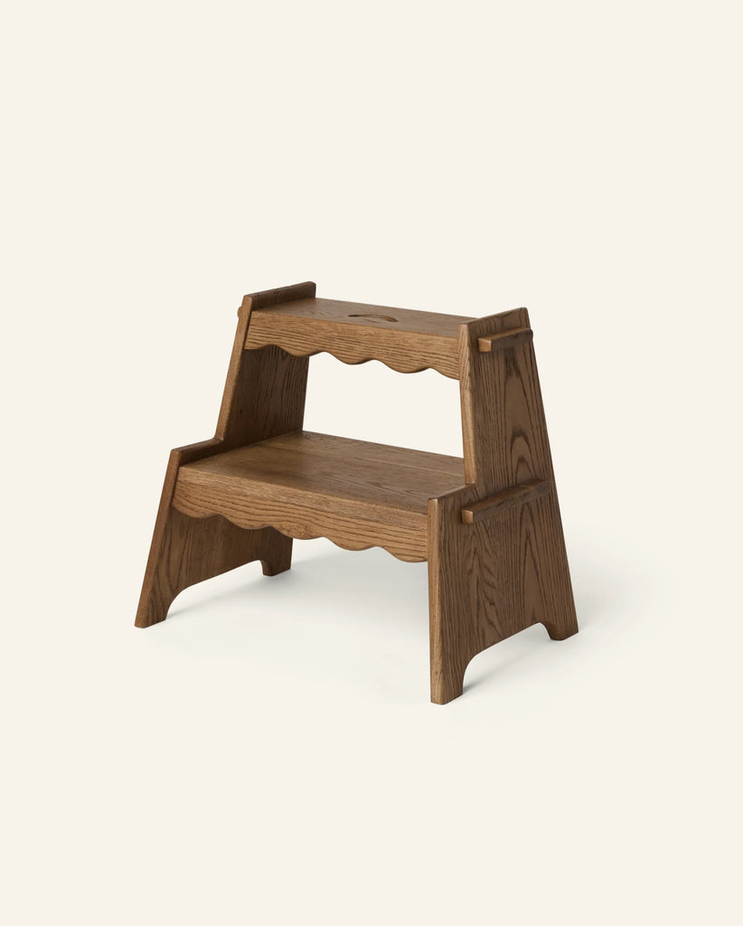 The Häti at Home - Margot Step Stool, a kids’ wooden two-step stool with scalloped edges and dark wood finish, stands on a plain light background.