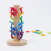 Grimm's Sorting Helper for Building Rings - Rainbow features a wooden stand with a vertical pole holding colorful building rings. Extra rings and tokens in vibrant hues are scattered on a white background.