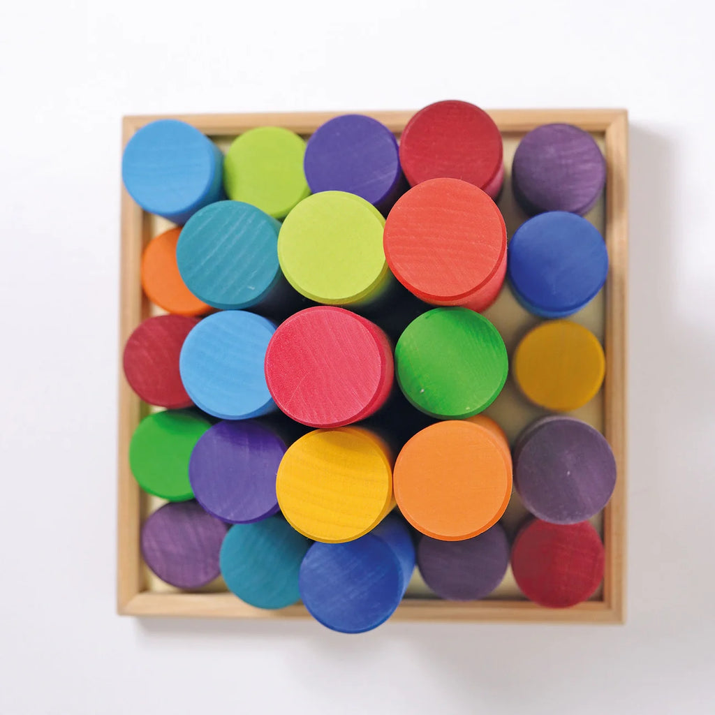 Grimm’s Large Building Rollers Rainbow featuring twenty-five multicolored wooden cylinders in a square wooden tray, designed for color sorting and motor skills development.