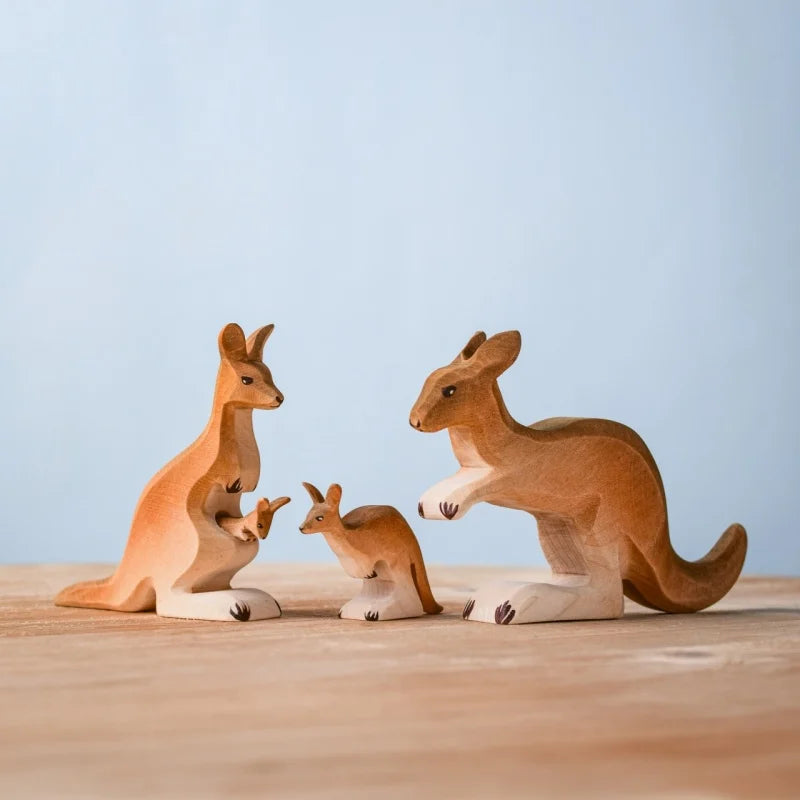 The Bumbu Wooden Kangaroo Family Set includes three sustainably crafted wooden figurines—two adults and a joey—on a light wood surface with a pale blue background. Perfect for Montessori-inspired play.