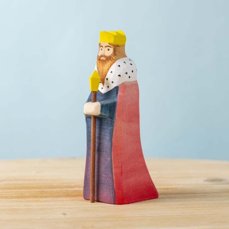 The Bumbu Handmade Wooden King features a yellow crown, red and blue robe, and white fur collar with black spots. He holds a staff and stands on light wood with a pale blue background—ideal for any medieval playset.