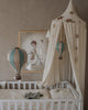 A cozy nursery corner featuring a white crib, cream canopy with gold stars, the Hot Air Balloon - Pastel Green ornament, and a framed child-on-bicycle illustration—ideal for anyone seeking handmade children's room decor.