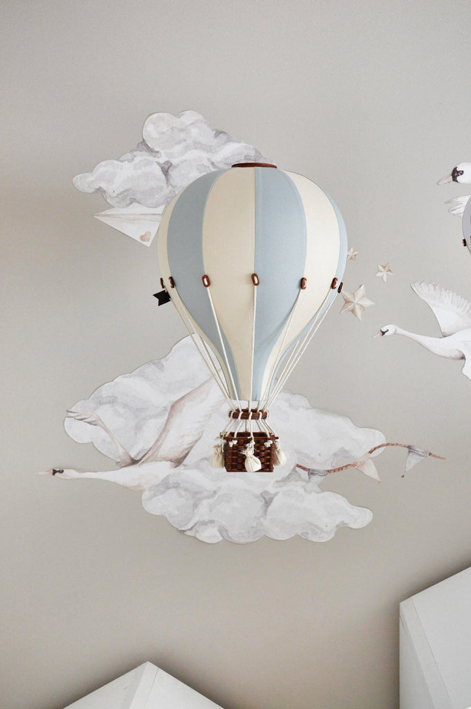 A handmade Hot Air Balloon - Beige / Mint / Grey model hangs against a wall with illustrated clouds, birds, and stars, creating a dreamy and whimsical decoration for children’s rooms.