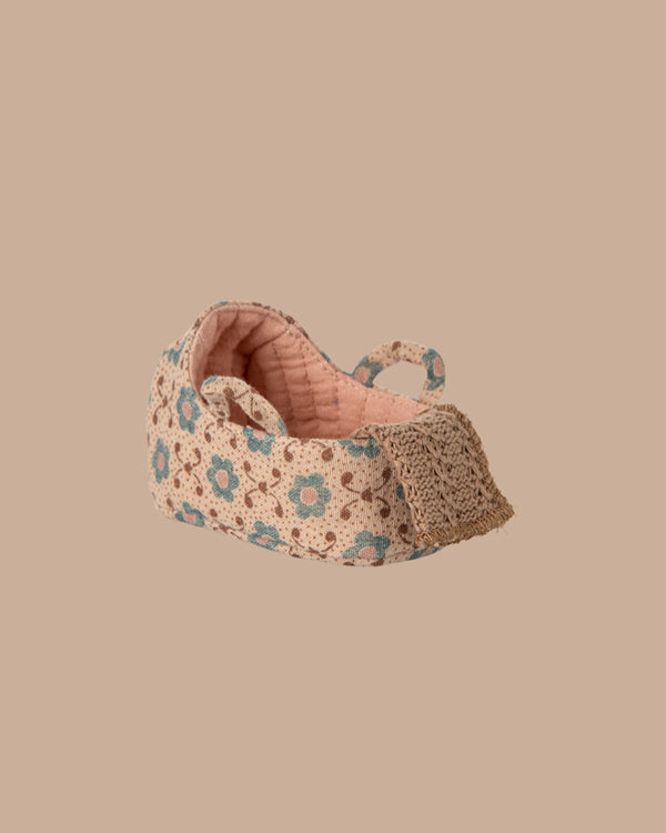 A small, fabric baby shoe with pink and beige tones, blue and brown florals, and lace detail—perfect for the PRE-ORDER: Carry Cot, Baby Mouse Size - Rose (ships late November)—displayed on a plain beige background.