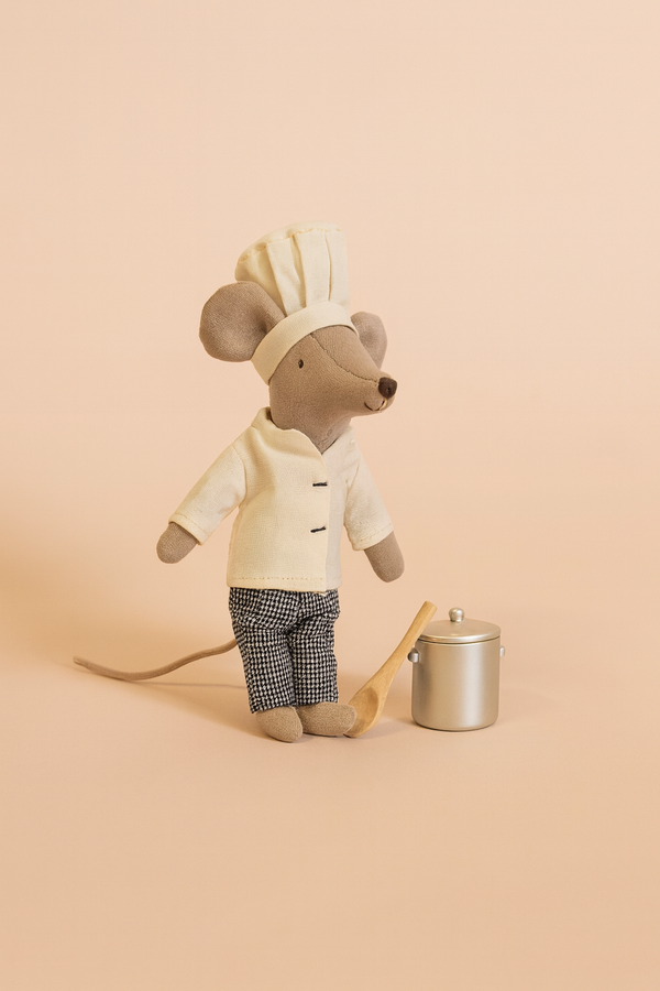 The Maileg Chef Mouse, dressed in a white jacket, checkered pants, and chef hat, stands beside a small silver pot and wooden spoon on a beige background.