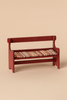 The Maileg Mouse Bench - Red is a small, hand-painted wooden bench with armrests and a backrest, featuring a striped cushion in beige, red, and green—ideal as charming mouse furniture—set against a plain beige background.