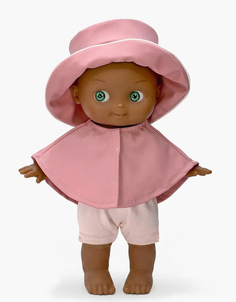 A high-quality vinyl Minikane Mini Pancha Doll - Prunelle with Pink Rain Suit, featuring dark skin, green eyes, a pink sun hat, a short pink cape, and pink shorts.