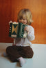 A young child sits on the floor playing a small green 10-key Konges Sloejd Accordian.