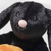 Close-up of Steiff Mr. Spice Hoppie Rabbit, a black Halloween plush with floppy ears, shiny black eyes, a soft pink nose, and velvety fur. A light brown object appears at the bottom of the image.