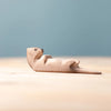 The Bumbu Handmade Wooden Otter Sleeping figure rests on its back atop a light wooden surface with a soft blue background, highlighting its eco-friendly craftsmanship.
