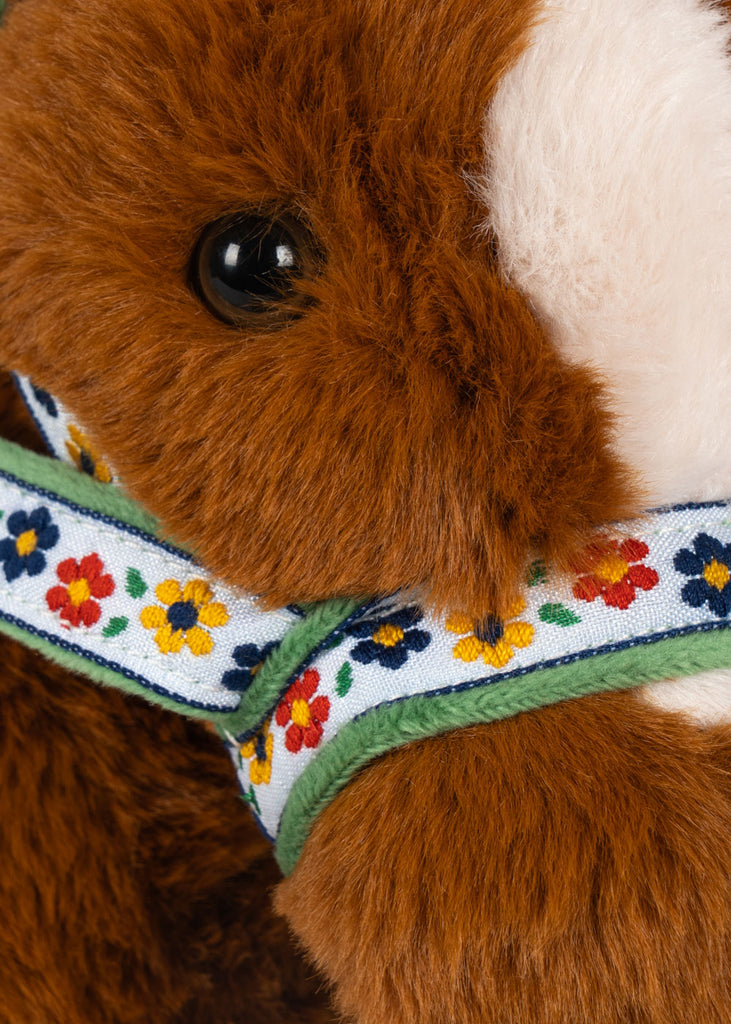 Close-up of a Konges Sloejd Fiona Horse, a soft brown plush pony featuring a bridle patterned with small blue, yellow, and red flowers.
