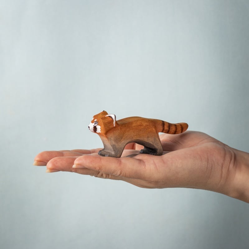 A hand holds a Bumbu Handmade Wooden Red Panda Family with Bamboo Set figure against a light blue background, ideal for Montessori learning toys or as part of the Red Panda Family collection.