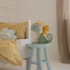The Handmade Wooden Lamp - Dragon, Hunter Green sits on a blue stool by a bed with yellow gingham bedding and plaid pillows, making charming nursery decor and a delightful children's night light in this cozy bedroom.