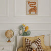 A cozy children's bedroom features a bed with yellow plaid bedding, a stuffed toy, a Handmade Wooden Lamp - Dragon, Hunter Green on the nightstand beside a globe, and a framed giraffe picture—perfect for charming nursery decor.