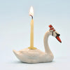 The Swan Cake Topper - Final Sale (ships in one week) is a hand-painted white ceramic swan with a red-striped party hat, holding a lit yellow candle on its back, set against a light blue background.