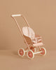 The Maileg Stroller, Micro - Powder is a small, pastel pink stroller with white wheels and a polka-dot fabric seat, shown against a beige background.