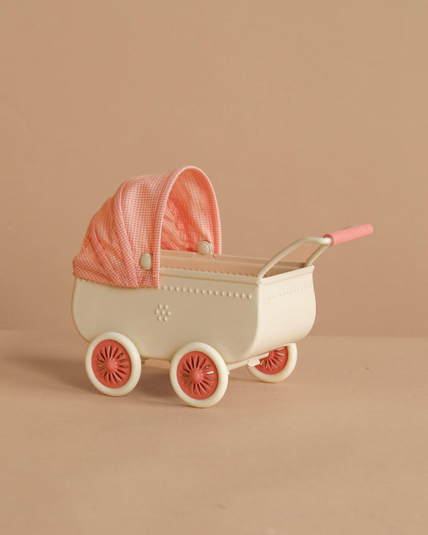 The Maileg Pram, Mouse - Coral features a vintage cream design with pink wheels and a pink checkered canopy, ideal for baby mice. Shown against a beige background.