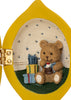 A Konges Sloejd Mini Surprise House - Lemon shaped hinged ornament opening to reveal a miniature world with a teddy bear holding a cupcake next to two wrapped gifts.