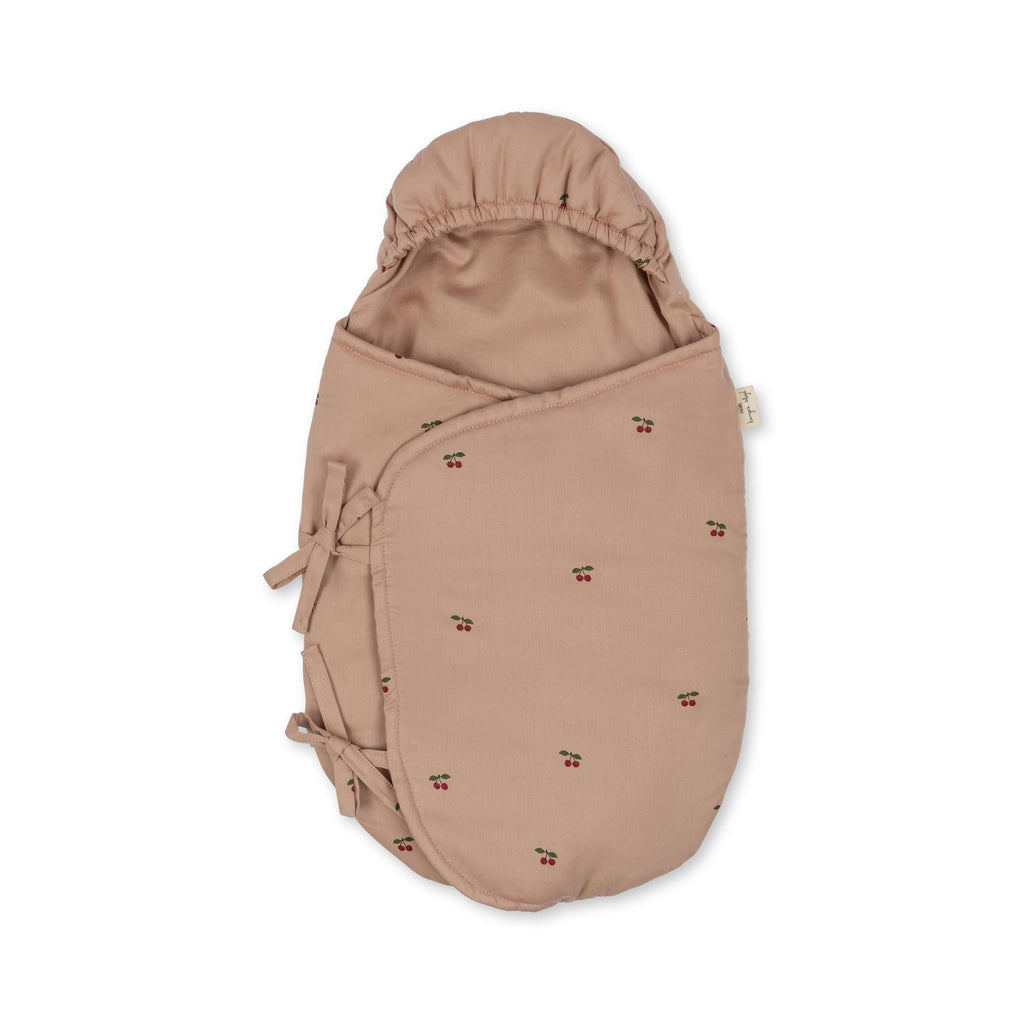 The Konges Sloejd Doll Sleeping Bag - Cherry Blush is a light brown, hooded sleeping bag with cherry prints, two side ties, and a soft organic cotton feel, shown against a white background.