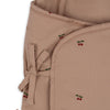 A close-up of the Konges Sloejd Doll Sleeping Bag - Cherry Blush, made from soft, light brown organic cotton with red cherry patterns, fabric ties, rounded edges, and recycled polyester filling.