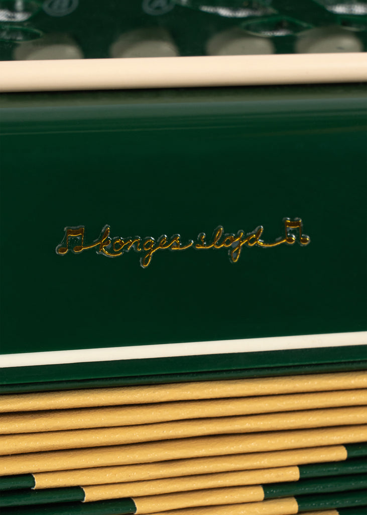 A close-up of a dark green Konges Sloejd Accordian featuring gold cursive text and a yellow pleated bellows section.