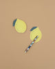 Two Lemon Sticky Notes in die-cut shapes and a multicolored pen are displayed on a plain light brown surface, with one sticky note placed above the pen and the other below it.