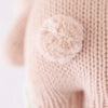 Close-up of a Cuddle + Kind Baby Bunny hand-knit fabric with a fluffy pom-pom attached, displaying a soft texture and detailed stitching.