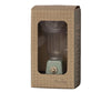 A small, mint green Maileg Miniature Blender is displayed in brown grid-patterned cardboard packaging with a clear plastic window. Perfect for children's toy collections and pretend play, the blender features a dial on the front. The packaging has text that reads "Maileg" and another text design along the side.
