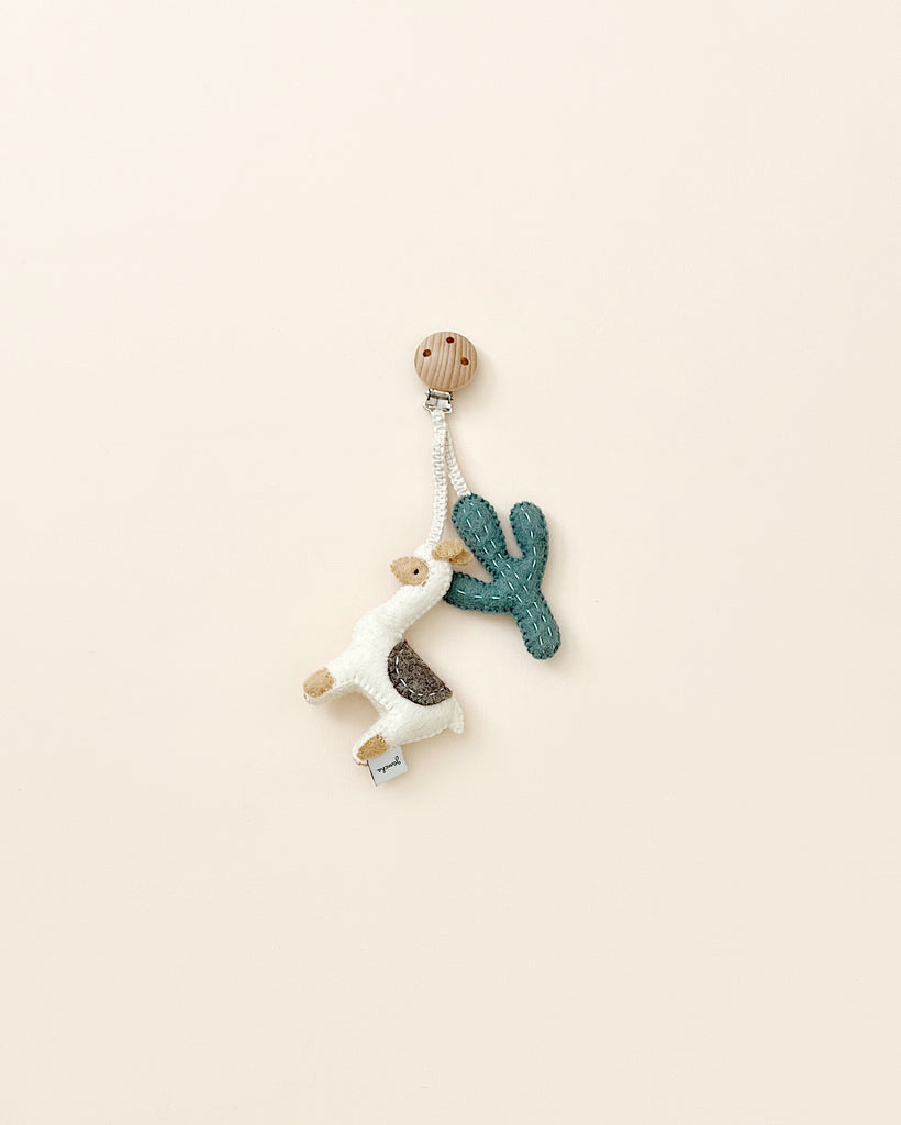 A handmade Llama Pram Clip with a wooden clasp, featuring soft wool llama and cactus charms, set against a plain beige background.