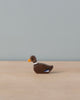 A Holztiger Swimming Duck, handcrafted from wood with a dark brown body, black and white neck markings, and an orange beak, is placed on a smooth, light-colored surface against a light grey background. Made in Europe by HOLZTIGER figures.