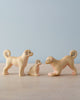 The Handmade Wooden Dog Family features three small ash wood dog figures—two adults and a puppy—displayed on a light surface with a pale blue background. One adult is in a playful pose. Eco-friendly, handcrafted toy made in Romania.