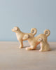 The Handmade Wooden Dog Family includes three small wooden dog figures of varying sizes, each with curled tails and simple facial features, displayed on a light wooden surface against a pale blue background.
